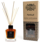 A "Patchouli" reed diffuser bottle and its brown cardboard box displayed side-by-side on a white background. The bottle contains a dark amber liquid, while the box shows the diffuser through a front window.