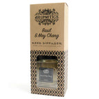 A brown cardboard box for a "Basil & May Chang" reed diffuser, standing upright on a white background. The box has a window that reveals the square glass bottle inside.