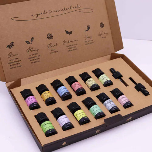 Open cardboard box set of 12 essential oils with colorful labels and two droppers, arranged neatly in a kraft insert, with illustrated guide to essential oil categories on the inside lid.