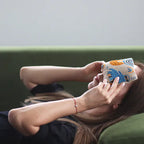 A woman is shown lying down on a green couch, using a blue and black spotted aromatherapy eye pillow for relaxation. This image highlights the soothing and therapeutic benefits of the eye pillow, enhancing the user's home fragrance and aromatherapy experience.