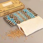 An eye-level shot showing a blue and black spotted aromatherapy eye pillow and its wheat-filled inner pouch. The box is visible in the background, showcasing the full package. This image is perfect for highlighting the natural components of a therapeutic home fragrance product.