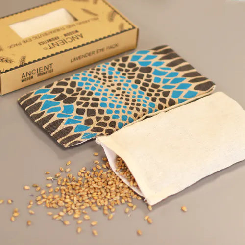 An eye-level shot showing a blue and black spotted aromatherapy eye pillow and its wheat-filled inner pouch. The box is visible in the background, showcasing the full package. This image is perfect for highlighting the natural components of a therapeutic home fragrance product.