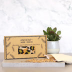 A clean product shot of a gift box for an aromatherapy eye pillow with a green and yellow leopard print. The box is placed on a modern surface, with wheat seeds and the inner pouch next to it, highlighting the natural materials used for this home fragrance and relaxation product.