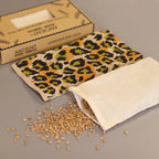 A close-up view of a green and yellow leopard-print aromatherapy eye pillow. The inner pouch, filled with wheat seeds, is pulled out of the case, demonstrating the product's natural filling and its use in creating a relaxing home fragrance and aromatherapy atmosphere.