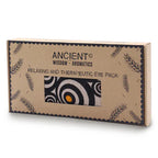 A product shot of a brown cardboard gift box for an aromatherapy eye pillow with a striking black, white, and orange spiral pattern. The box is clearly labeled "Ancient Wisdom - Aromatics" and "Relaxing and Therapeutic Eye Pack," promoting a soothing home fragrance and aromatherapy experience.