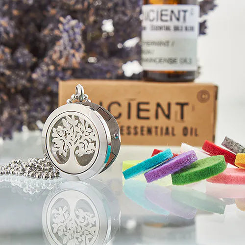 Silver Tree of Life essential oil diffuser pendant necklace with colorful felt pads, lavender flowers, and Ancient Wisdom essential oil bottle in the background.