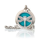 A close-up of a decorative, round silver-colored charm with an dragonfly pattern in the centre. This piece of aromatherapy jewelry is designed to diffuse essential oils, allowing the wearer to carry their favorite fragrance with them.