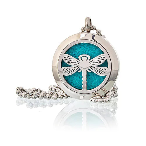 A close-up of a decorative, round silver-colored charm with an dragonfly pattern in the centre. This piece of aromatherapy jewelry is designed to diffuse essential oils, allowing the wearer to carry their favorite fragrance with them.