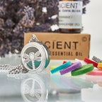 Stainless steel diffuser necklace with dragonfly cut-out pendant, shown with colorful felt pads and essential oil bottle in the background.