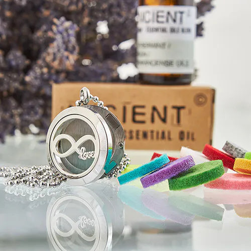 Stainless steel aromatherapy pendant with infinity love symbol, displayed with colorful felt pads and essential oil background.