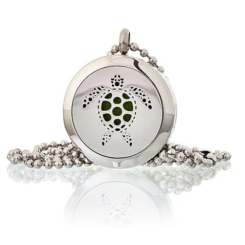 A product shot of a silver-colored essential oil diffuser necklace, featuring a delicate chain and a round charm with a turtle filigree design. The charm is designed to hold essential oils, offering a stylish way to enjoy aromatherapy.