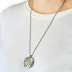 Model wearing a silver essential oil diffuser necklace with a leaves design and green felt insert, paired with a plain white shirt.