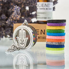 Silver Hamsa hand essential oil diffuser pendant necklace shown next to colorful felt pads and lavender in the background.