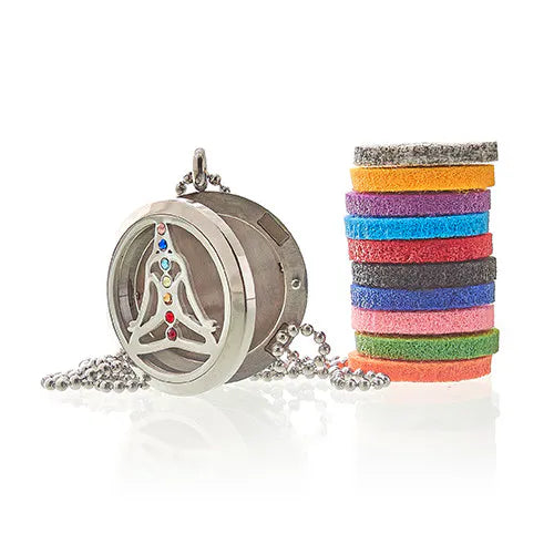 Stainless steel aromatherapy locket pendant with a meditating yoga figure inlaid with colorful chakra crystals, displayed next to a stack of multicolored felt pads.
