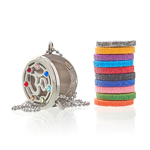 Stainless steel aromatherapy locket necklace with Om symbol and colorful gemstones, displayed next to a stack of multicolored felt pads.