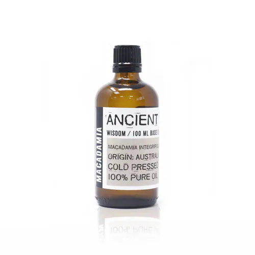 Amber glass bottle labeled “Ancient Wisdom / 100 ml Base Oil.” The label specifies “Macadamia Integrifolia,” origin Australia, cold pressed, and 100% pure oil. The bottle has a black screw cap and a minimal white and gray label design with “Macadamia” written vertically on the side.
