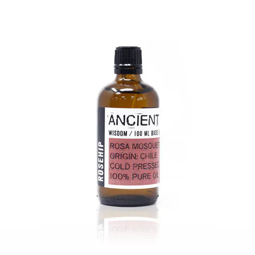 Amber glass bottle labeled “Ancient Wisdom / 100 ml Base Oil.” The front label specifies “Rosa Mosqueta,” origin Chile, cold pressed, and 100% pure oil. The central part of the label is red with black printed text, while the word “Rosehip” appears vertically on the left side in bold white letters. The bottle is sealed with a black screw cap, presenting a minimal and apothecary-inspired design.