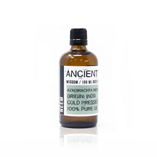 Amber glass bottle labeled “Ancient Wisdom / 100 ml Base Oil.” The front label identifies the product as “Azadirachta Indica” (Neem oil), origin India, cold pressed, and 100% pure oil. The central part of the label is pale green with black printed text, while the word “NEEM” appears vertically in bold white letters on the left side. The bottle has a black screw cap and a minimalist apothecary-style design.