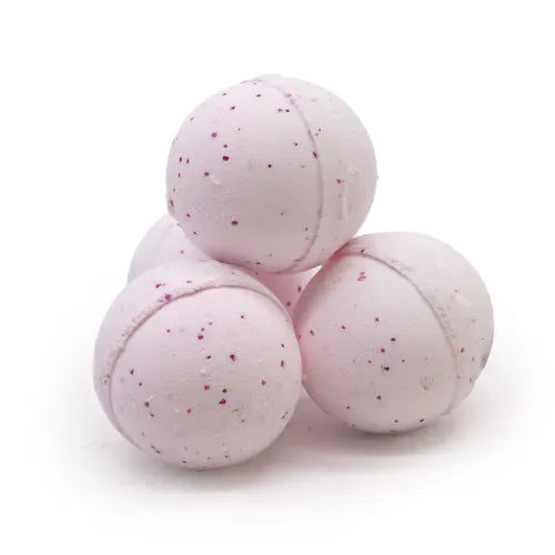 Four light pink bath bombs stacked together in a pyramid. Their smooth surface is dotted with small dark pink speckles, giving them a delicate and playful appearance. The texture suggests a fizzy, aromatic experience when dissolved in water.