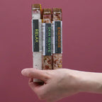 Hand holding three tubes of aromatherapy bath salts against a pink background