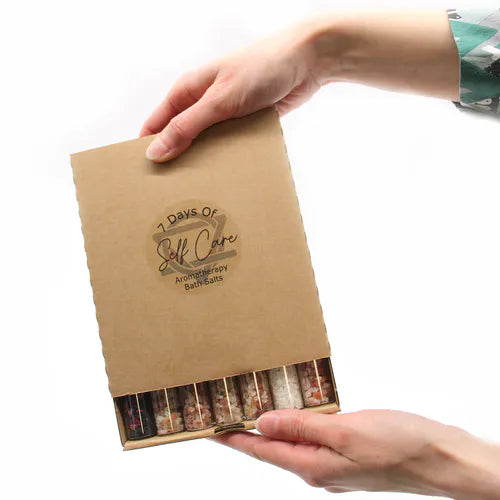 Person holding a cardboard box labeled "7 Days of Self Care Aromatherapy Bath Salts"