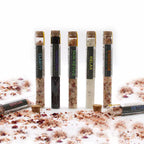 Seven glass tubes of aromatherapy bath salts displayed with scattered salt and petals