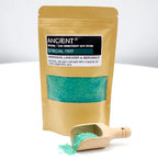 Ancient Wisdom Aromatherapy Bath Potion "Special PMT" in a kraft resealable pouch filled with teal bath salt, shown with a small wooden scoop placed in front. Some of the teal bath salt spills out of the scoop, emphasizing the texture of the natural crystals.
