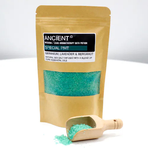 Ancient Wisdom Aromatherapy Bath Potion "Special PMT" in a kraft resealable pouch filled with teal bath salt, shown with a small wooden scoop placed in front. Some of the teal bath salt spills out of the scoop, emphasizing the texture of the natural crystals.