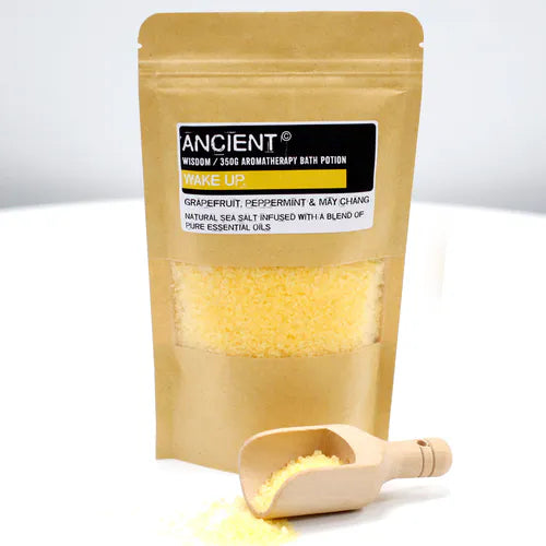 Kraft paper pouch with yellow bath salts, labeled "Ancient Wisdom Aromatherapy Bath Potion – Wake Up", shown with a small wooden scoop filled with salts.