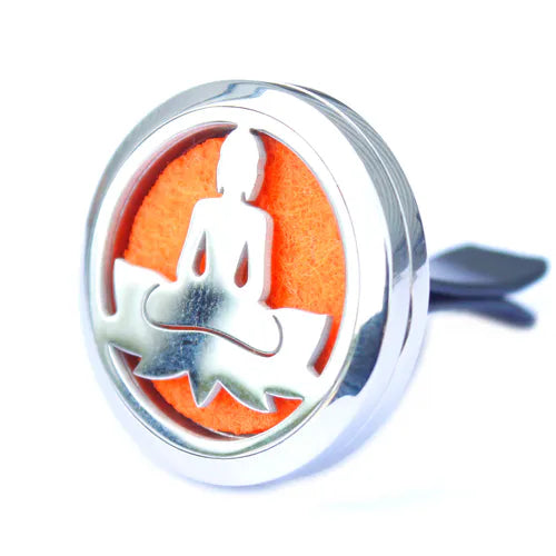 Close-up of a silver car air diffuser with an intricate cut-out design of a meditating Buddha sitting on a lotus flower. The bright orange felt pad inside adds a vibrant and energizing touch, symbolizing balance and mindfulness while keeping the car fresh.