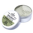 Open tin of Ancient Wisdom Earth Clay Mask containing fine pale green clay powder. The silver container has the lid leaning against it, showing the green and white product label with benefits listed as “tightens” and “refreshes.”