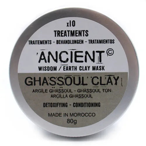 Round metal tin of Ancient Wisdom Earth Clay Mask labeled "GHASSOUL CLAY." The label indicates detoxifying and conditioning properties, made in Morocco, 80g. The lid is fully closed, showing the text clearly in black on a beige and white background.