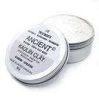 Open tin of Ancient Wisdom Earth Clay Mask with Kaolin Clay. The round silver metal container is shown with the lid tilted to the side, revealing the fine white clay powder inside. The label on the lid reads “x10 Treatments, Ancient Wisdom Earth Clay Mask, Kaolin Clay, Cleansing - Exfoliating, Made in United Kingdom, 50g” in bold black text with translations in French, German, and Spanish.