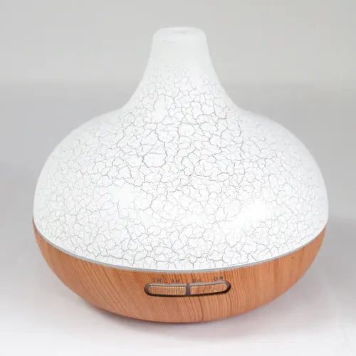 A product shot of a round essential oil diffuser with a white cracked-pattern top and a light wood grain base. It has buttons for controlling the timer and power, and is on a white background.