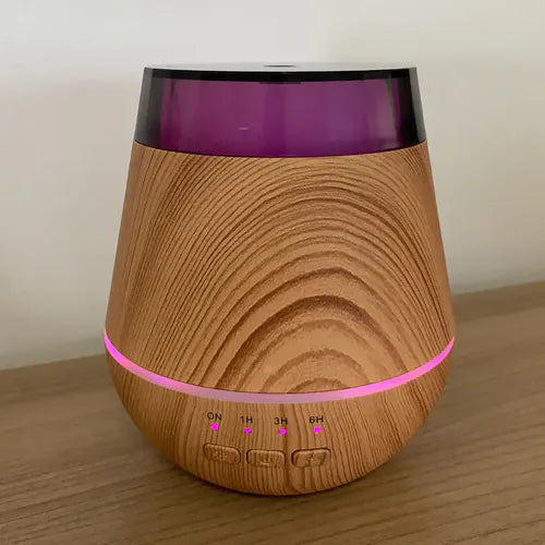 Wood grain aroma diffuser placed on a wooden surface, illuminated with a pink LED ring light and active timer indicators for ON, 1H, 3H, and 6H beneath three control buttons.