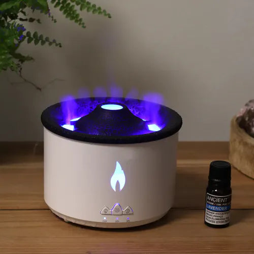 White cylindrical aroma diffuser with glowing blue light and mist effect from the top, placed on a wooden surface next to a lavender essential oil bottle.