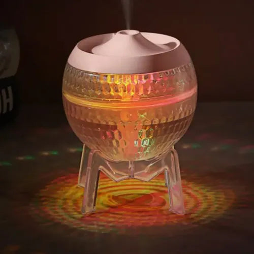 Spherical glass aroma diffuser with a pink lid, lit up with warm yellow, red, and green LED lights, placed on a clear tripod stand.