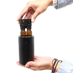 Hands inserting two amber glass bottles into the portable black aroma diffuser.