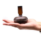 Hand holding a small wood grain essential oil diffuser with an amber glass bottle attached upside down on top.