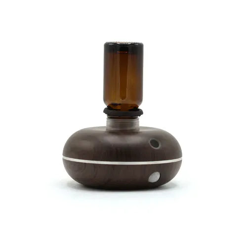 Close-up of a wood grain essential oil diffuser with an amber glass bottle inserted upside down on top.