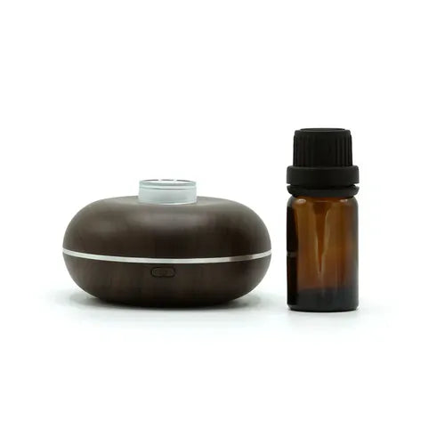 Compact wood grain essential oil diffuser with an amber glass essential oil bottle placed beside it on a white background.
