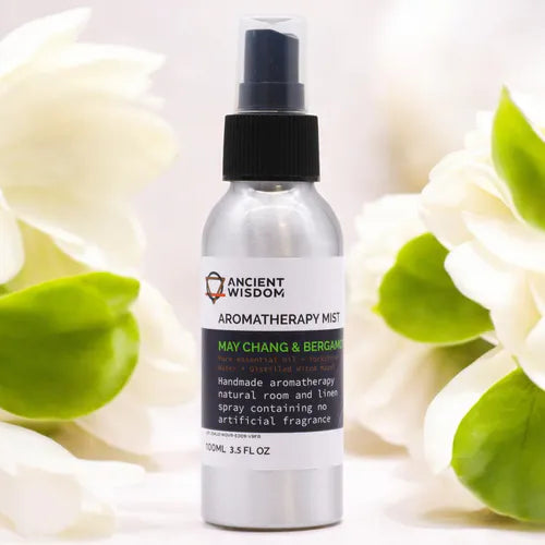 Aluminum spray bottle labeled “Ancient Wisdom Aromatherapy Mist – May Chang & Bergamot.” The 100ml (3.5 fl oz) bottle has a white label with black and green text, black spray cap, and is displayed among soft white flowers and green leaves, creating a fresh and natural atmosphere.