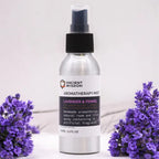 A silver aluminum spray bottle labeled "Ancient Wisdom Aromatherapy Mist – Lavender & Fennel," placed on a light surface surrounded by fresh lavender flowers. The label highlights it as a handmade natural room and linen spray with essential oils, Yorkshire water, and witch hazel, free from artificial fragrance. The purple lavender flowers in the foreground and background accentuate the calming and herbal essence of the product.