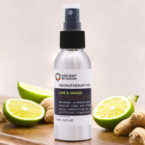 Silver spray bottle of Ancient Wisdom Aromatherapy Mist labeled "Lime & Ginger," displayed with fresh lime halves and ginger roots.