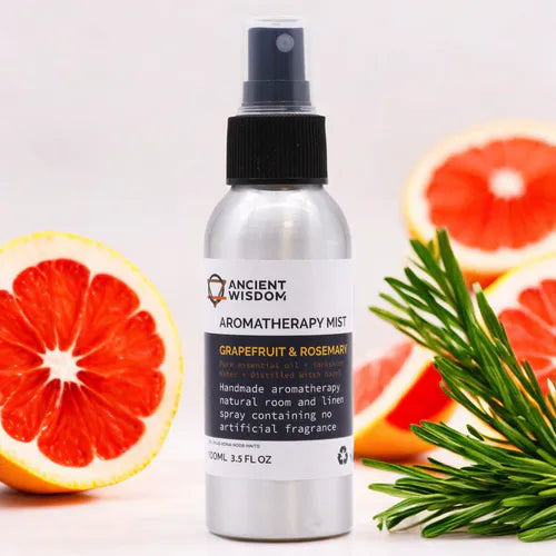 100 ml aluminum spray bottle from Ancient Wisdom Aromatherapy Mist Grapefruit & Rosemary, positioned in the center with natural decorations around: fresh grapefruit slices and a sprig of green rosemary. The background is clear and bright, creating a fresh and natural atmosphere that recalls the main ingredients of the product.