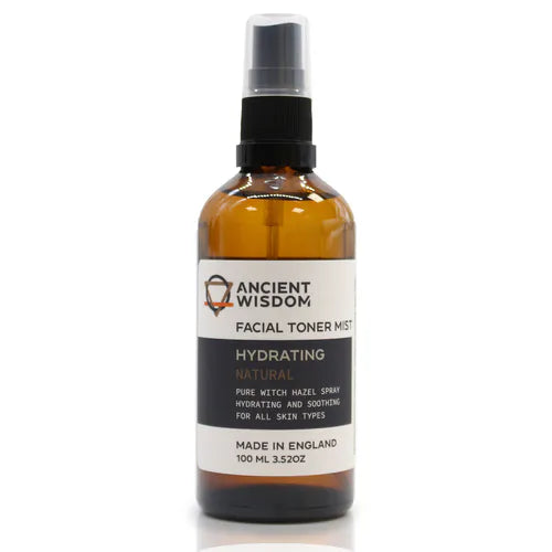 Brown glass spray bottle labeled "Ancient Wisdom Facial Toner Mist Hydrating Natural," featuring witch hazel extract. The white and black label indicates it is hydrating and soothing for all skin types. Bottle shown upright with black spray cap.