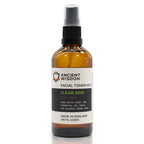 Brown glass spray bottle of "Ancient Wisdom Facial Toner Mist Clear Skin Tea Tree," upright with black spray cap. The label states it is designed with tea tree and witch hazel to help treat blemish-prone skin.