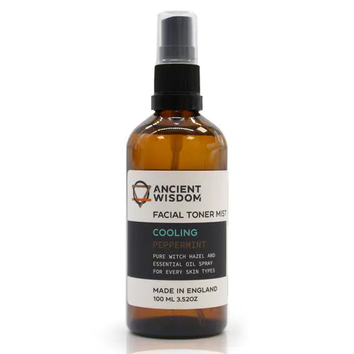 Brown glass spray bottle labeled "Ancient Wisdom Facial Toner Mist Cooling Peppermint," with a black spray cap and white label. The label highlights peppermint and witch hazel as ingredients, designed for refreshing and soothing all skin types.