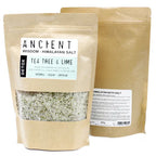 Brown kraft pouch of Ancient Wisdom Himalayan Bath Salt Tea Tree & Lime, detox blend with essential oils, evening primrose oil, and dry herbs; coarse Himalayan salt visible with green herbal pieces.