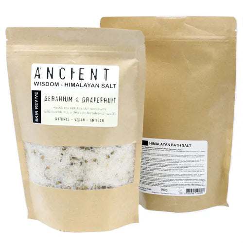 Brown kraft pouch of Ancient Wisdom Himalayan Bath Salt Geranium & Grapefruit, skin revive formula enriched with essential oils, vitamin E oil, and chamomile flowers; pale coarse salt with yellow botanical specks visible.